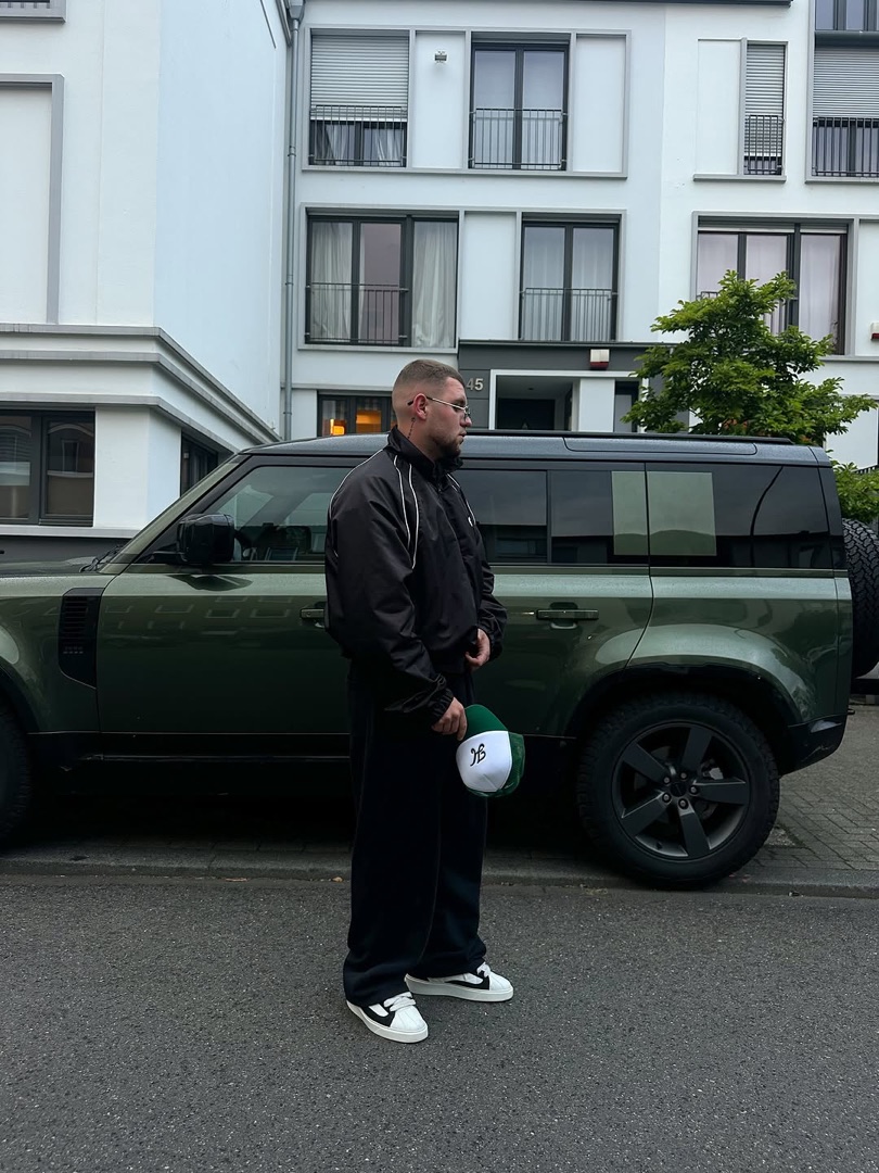 Gregor in Schwarz vor einem grünen Geländewagen
