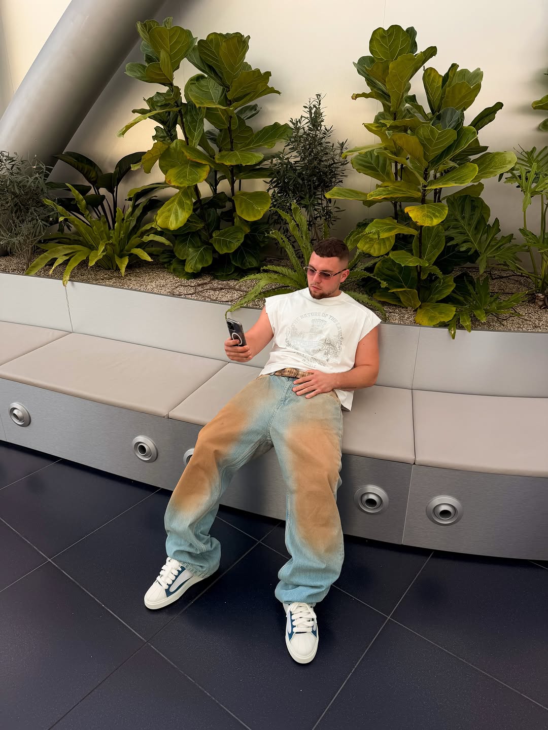 Gregor sitzt mit Smartphone vor einer Pflanzenwand, Outfit von Klyde